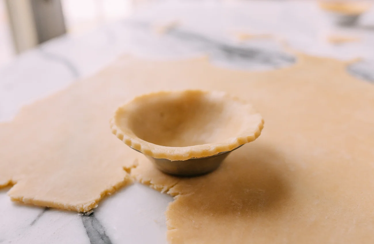 Pressing dough into tart tin with lip over edge